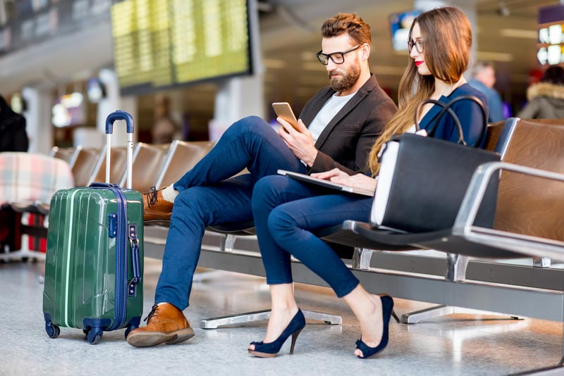 Elegante casal de negócios sentado com telefone e livro na sala de espera no aeroporto.