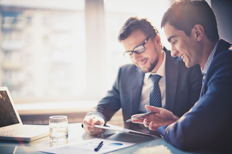 Imagem de dois jovens empresários usando touchpad na reunião.