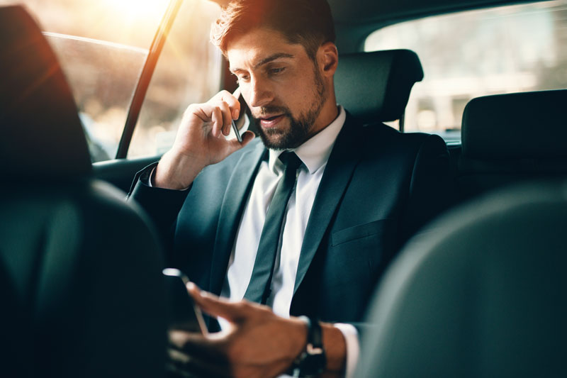 Jovem empresário falando no telefone celular e usando tablet pc enquanto sentado no banco de trás de um carro