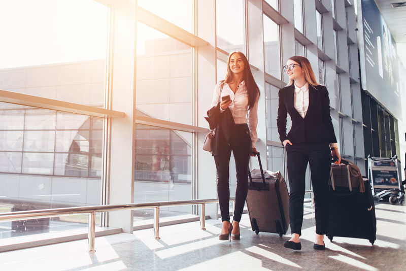 Dois parceiros de negócios sorridentes indo em viagem de negócios transportando malas enquanto caminham pela passagem do aeroporto.