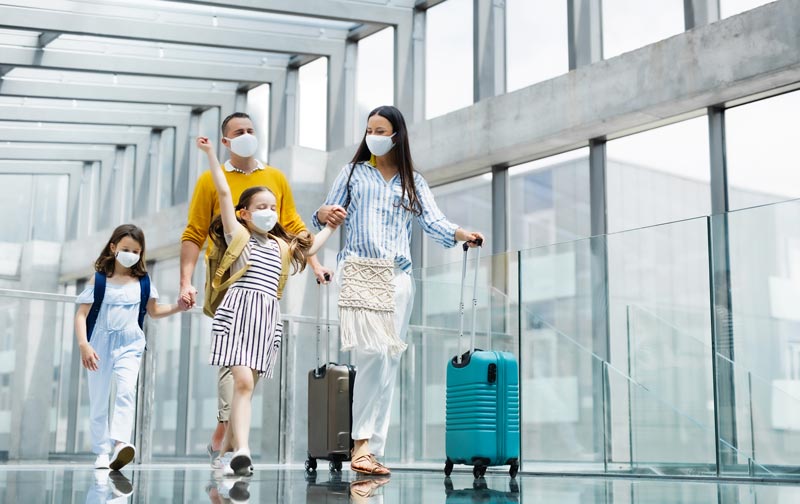 Família com dois filhos saindo de férias, usando máscaras faciais no aeroporto.