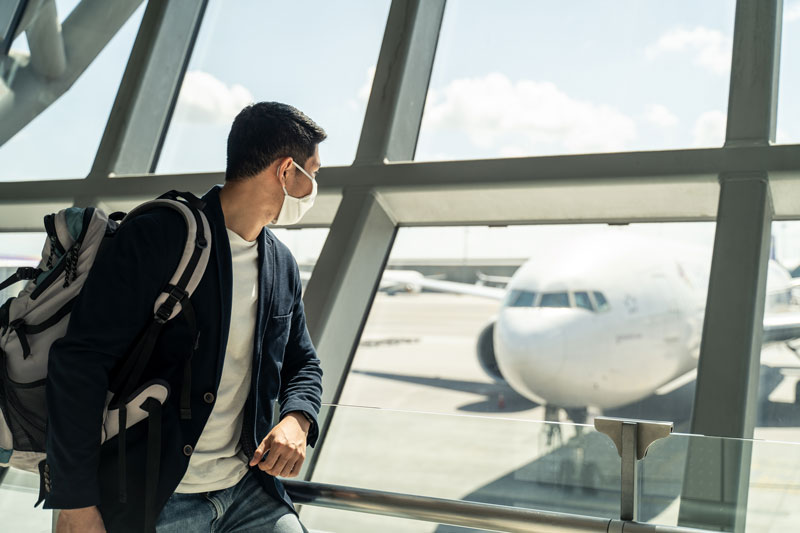 Homem de negócios viajante asiático usando máscara facial esperando para embarcar no avião, parado no terminal de partida no aeroporto.