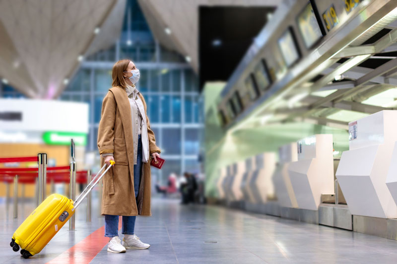 Mulher com bagagem fica em balcões de check-in quase vazios no terminal do aeroporto devido a restrições de viagem de surto coronavírus/Covid-19.