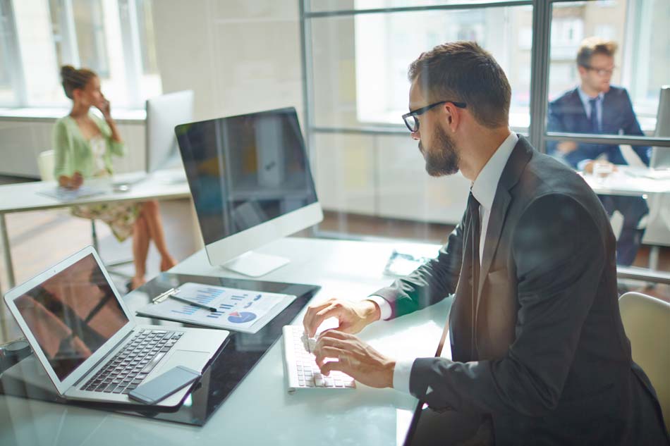 Jovem empregado olhando para monitor de computador durante o dia de trabalho no escritório.